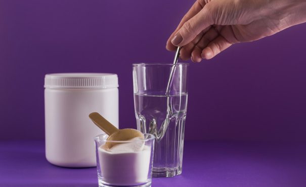 glass-with-collagen-dissolved-in-water-and-collage-2025-03-18-15-54-11-utc Glass with collagen dissolved in water and collagen protein powder on purple background. Woman's hand holds a spoon. Healthy lifestyle concept.