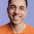 Young brunette white man smiling and looking at camera Young brunette white man smiling and looking at camera isolated over purple background