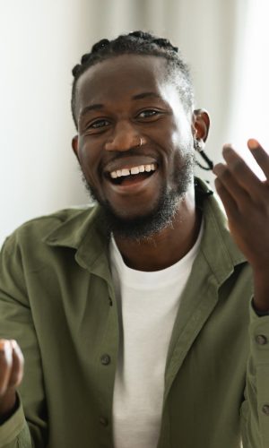 Video call concept. Happy african american man talking to camera, gesturing and smiling, sitting at workplace at home. Modern remote communication and e-teaching