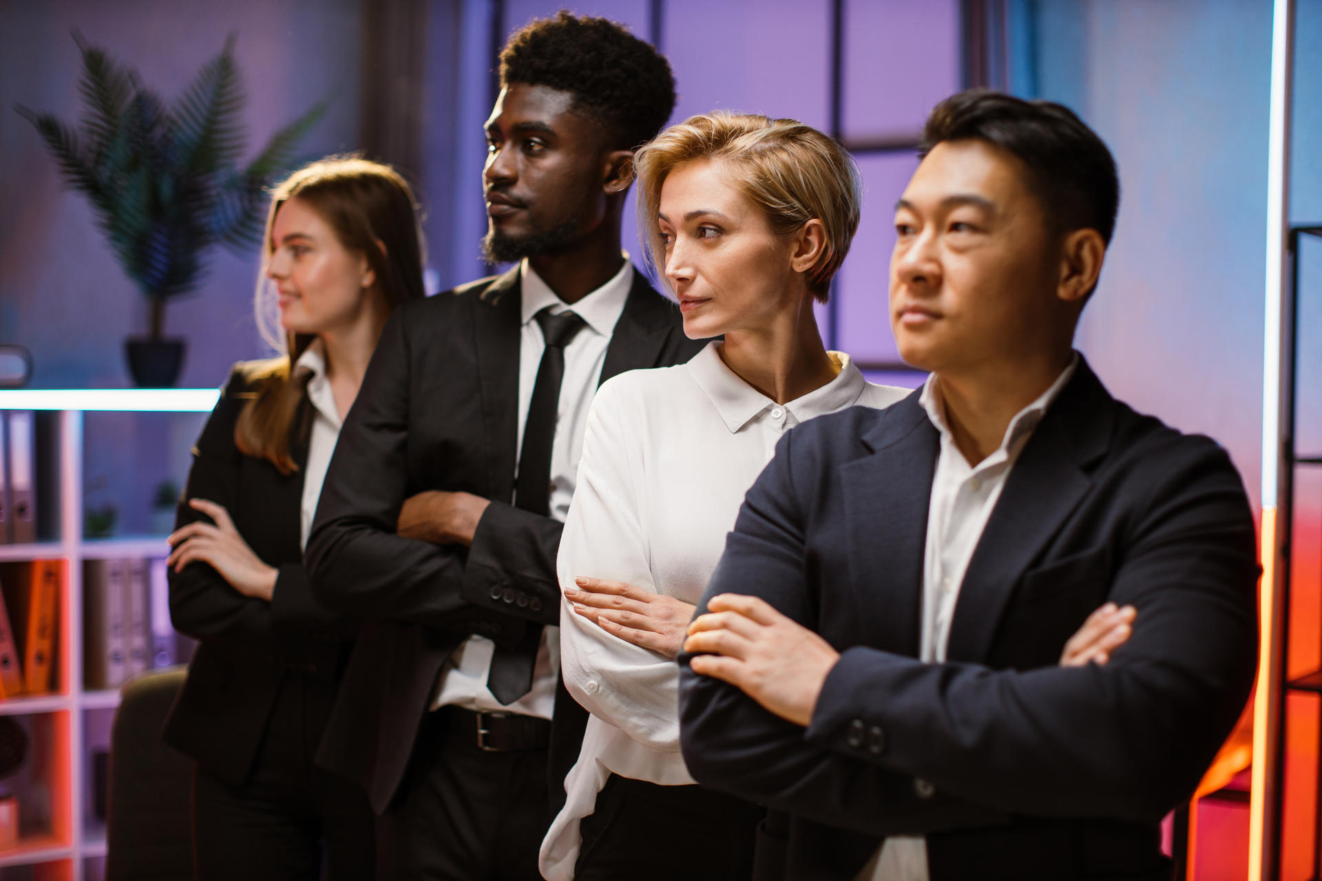 Smart confident business team in formal suits are looking away while standing in a row with crossed arms in office. Focus on pretty blond Caucasian lady in white shirt