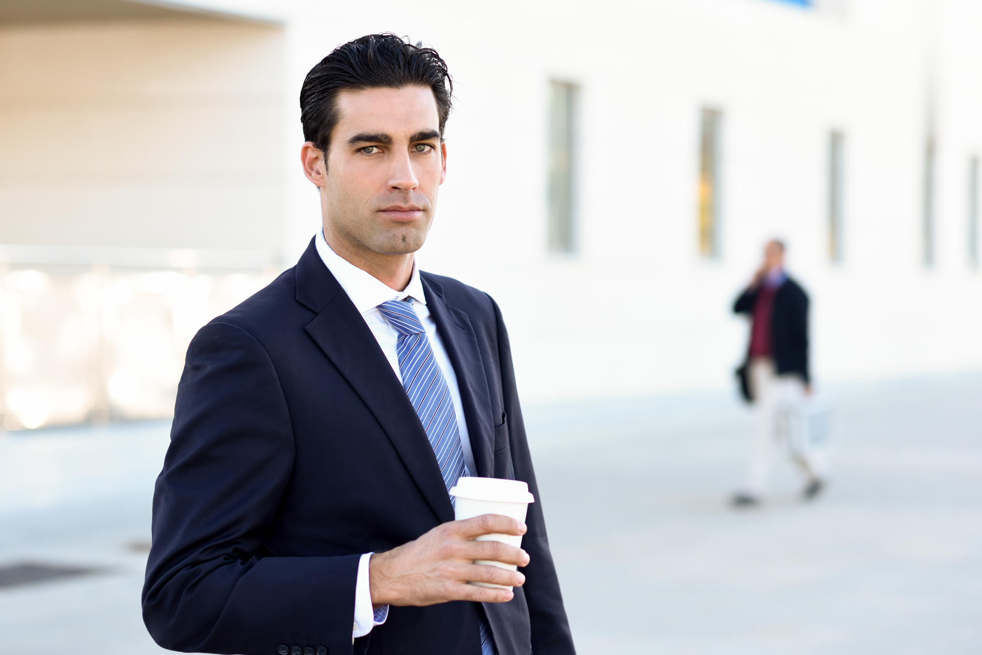 Businessman drinking coffee to go with a take away cup Businessman with formal clothes drinking coffee to go with a take away cup. Man wearing blue suit and tie in urban background.
