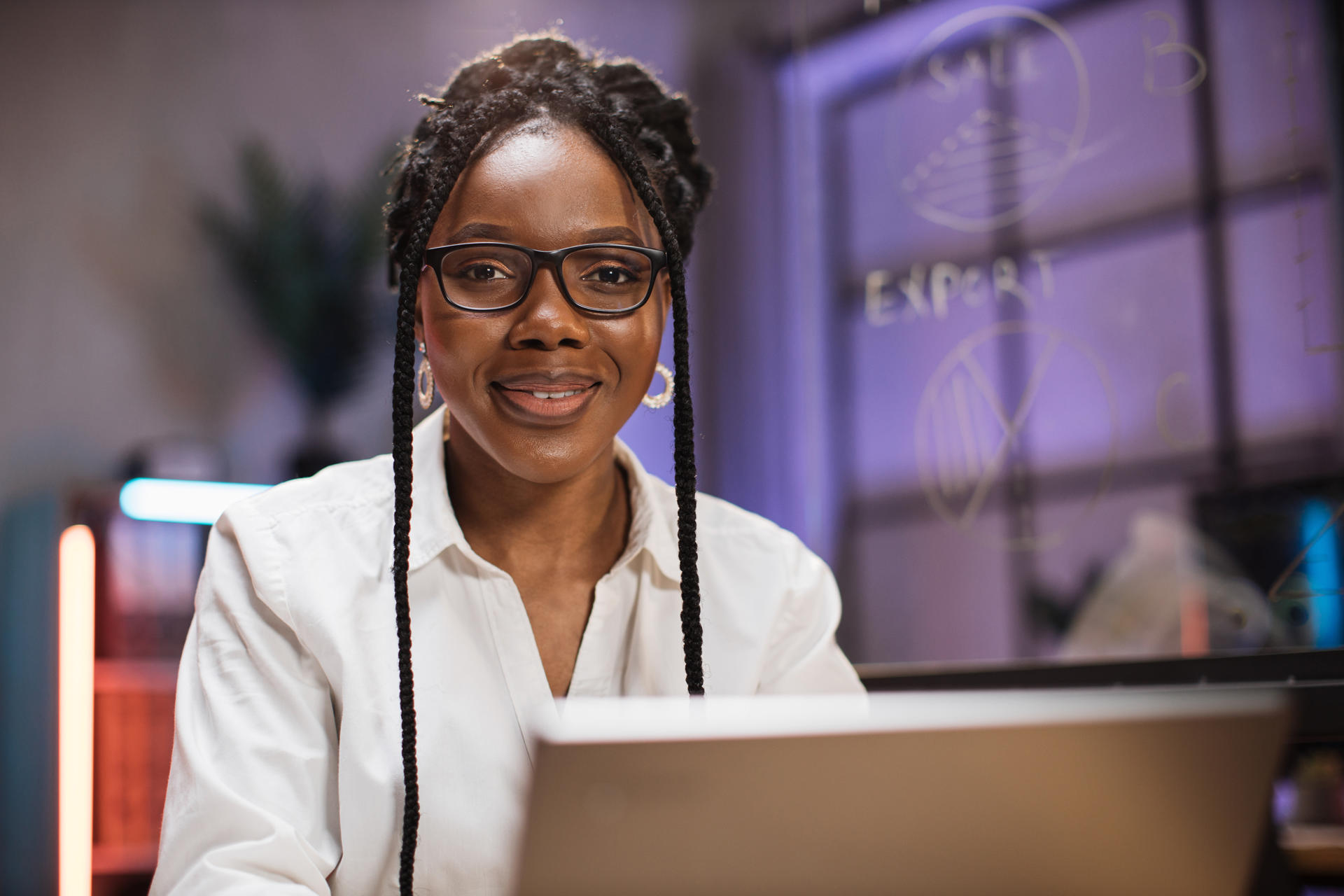 African american woman in formal wear sitting at desk and looking at modern laptop computer with serious facial expression. Concept of people and office work.