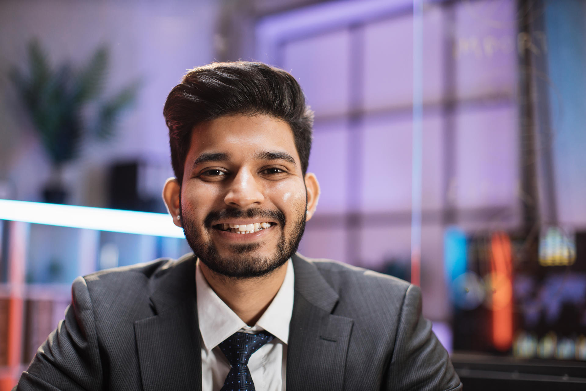 Smiling positive confident indian man in formal wear sitting at office desk. Company worker with beard looking at camera. Concept of people and business.