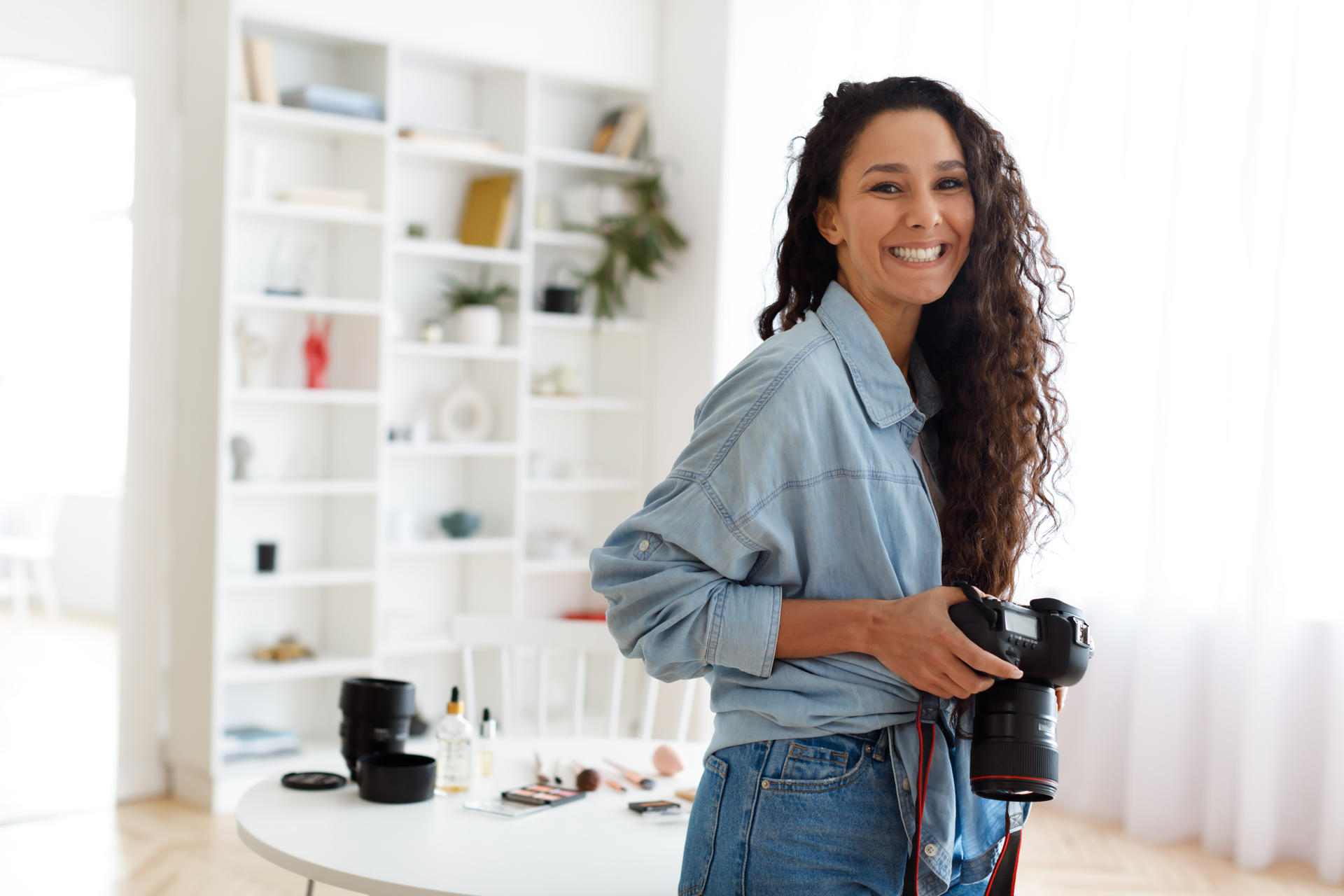 Female Photographer Posing Holding Photocamera Standing In Modern Studio Photography Career. Female Photographer Posing Holding Photocamera Smiling Looking At Camera Standing In Modern Studio Indoors. Creative Professions And Photo Art Concept