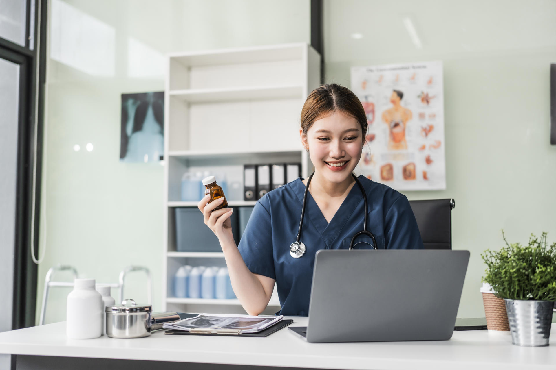 A young Asian nurse providing online consultations, seated at her desk with a laptop. She offers