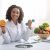 Sport and vitamins for immunity. Happy black woman doctor holding orange and barbell in clinic, posing at her workplace, free space