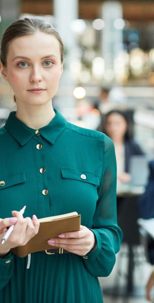 Portrait of Young Woman in Office Building Waist up portrait of young businesswoman holding planner and looking at camera in office building interior, copy space