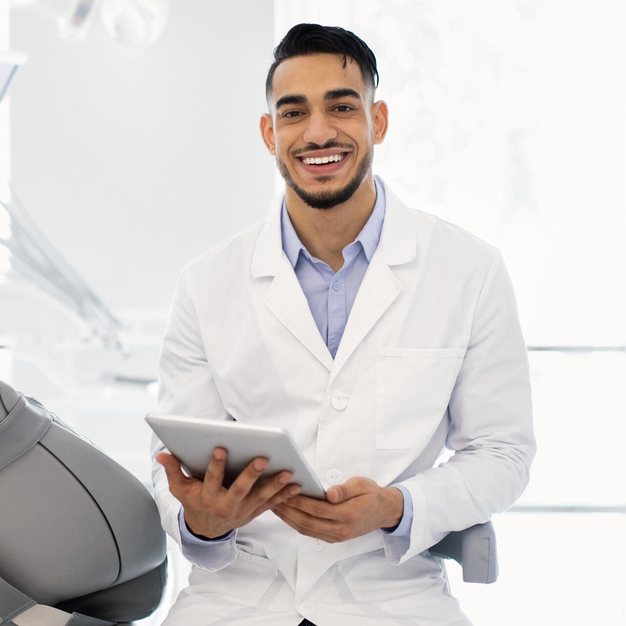 Modern Dentistry. Portrait Of Young Arab Stomatologist Using Digital Tablet At Workplace Modern Dentistry. Portrait Of Young Arab Male Stomatologist Using Digital Tablet At Workplace In Dental Clinic, Handsome Middle Eastern Dentist Waiting For Patient, Ready For Check Up, Copy Space