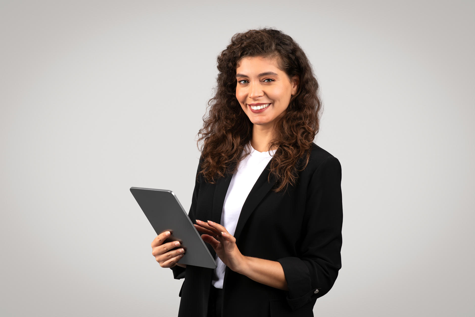 Confident young businesswoman with curly hair smiling and holding digital tablet, representing modern professionalism and technology in business