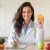 Attractive european nutrition adviser holding orange and making meal plan for client, working at weight loss clinic Attractive young european nutrition adviser holding orange and making meal plan for client, working at weight loss clinic. Smiling female dietitian writing prescription for patient