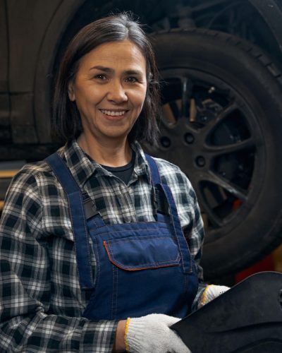 Amicable lady enjoying working as a car technician Joyful brunette car mechanic holding equipment and smiling at the camera